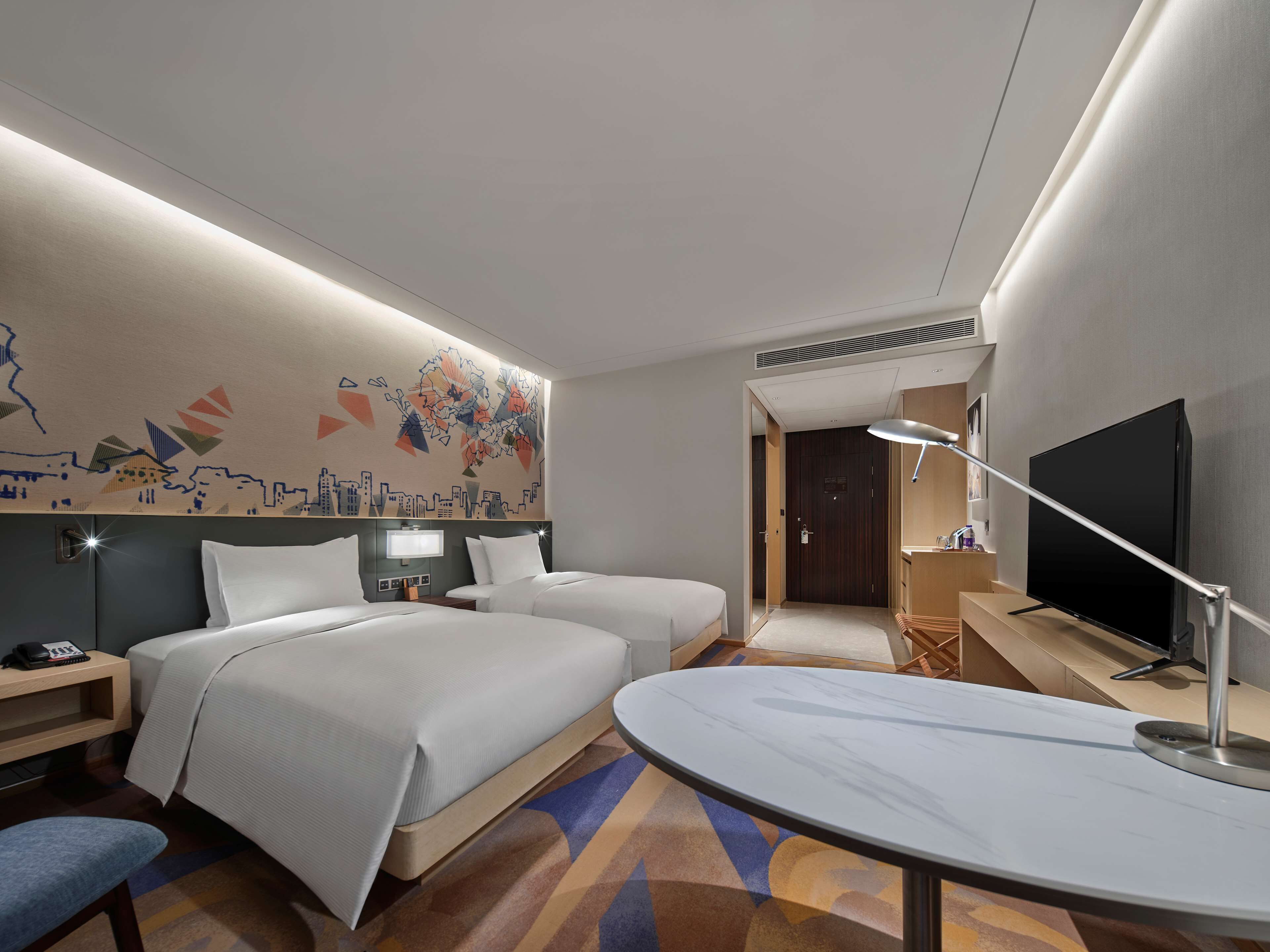 Une chambre d’hôtel avec deux lits, un bureau, une chaise, un téléviseur à écran plat et une fresque murale.