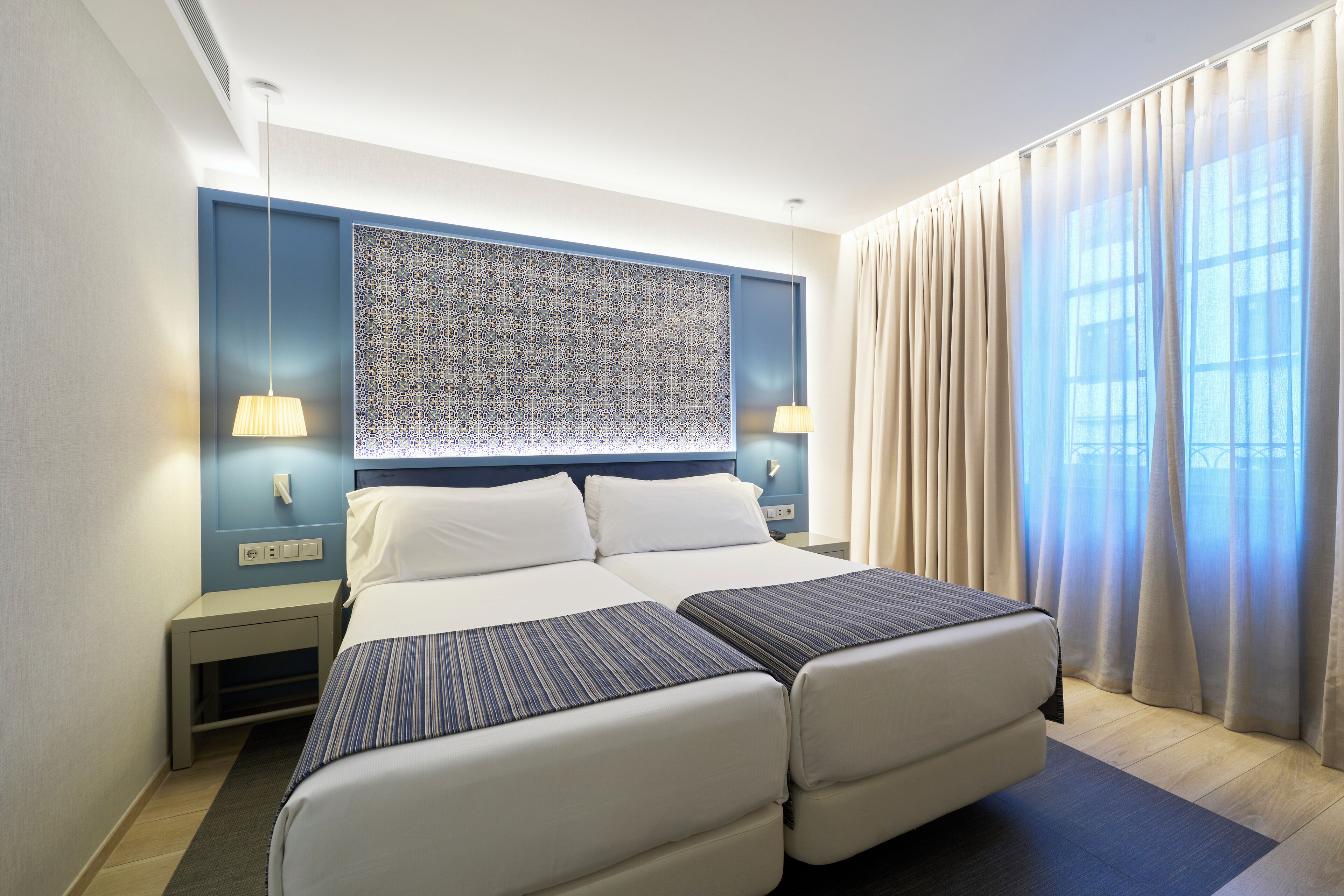 A hotel room with a large bed, two bedside tables, a wall-mounted artwork, and a window with curtains.
