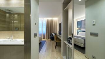 Quarto de hotel moderno com um espelho grande, mesa de cabeceira, cama e banheiro com pia e chuveiro.