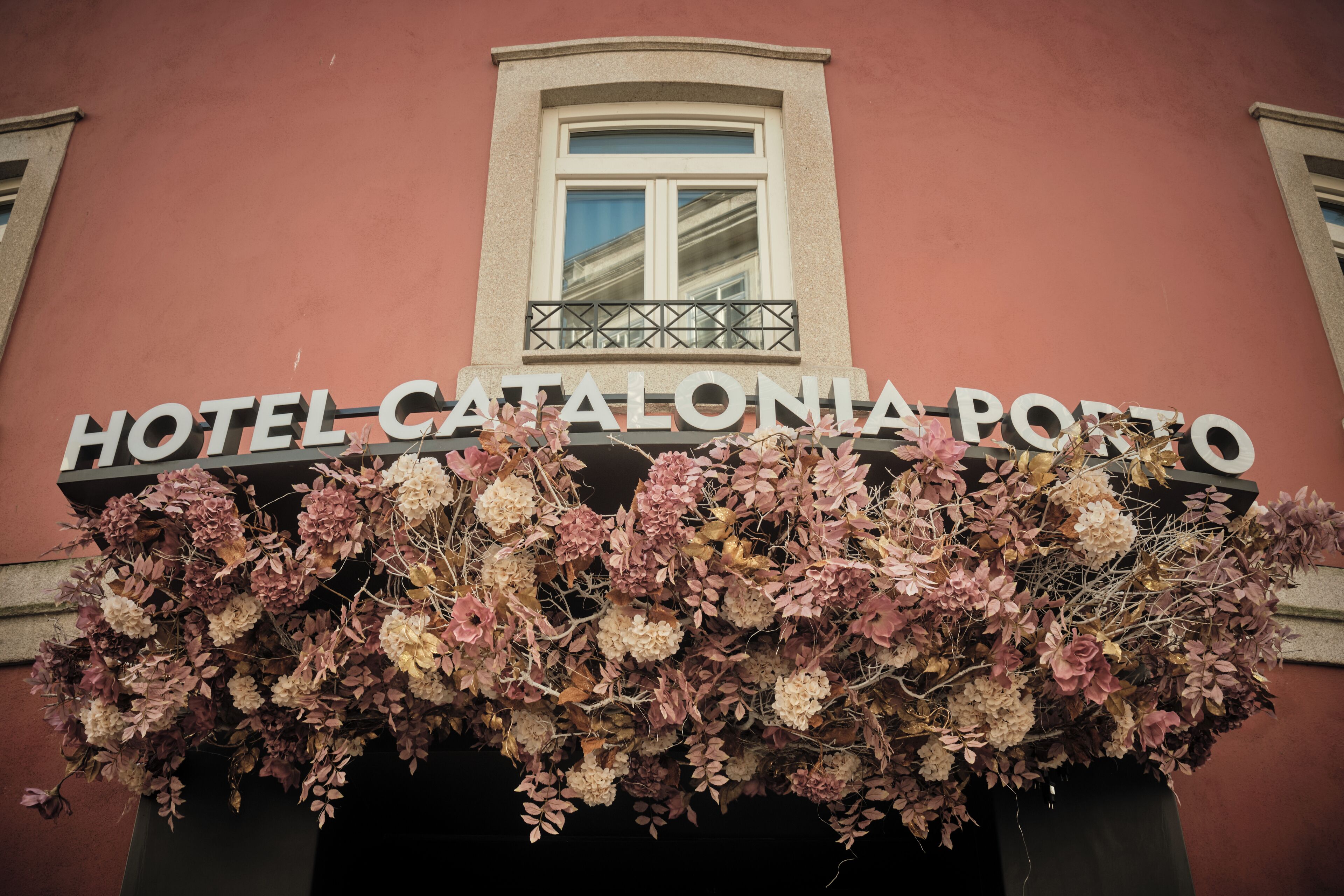The exterior of Hotel Catalonia Porto with a sign above the entrance and a floral arrangement below.