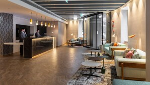 A modern hotel lobby with a reception desk, seating area, and large windows.