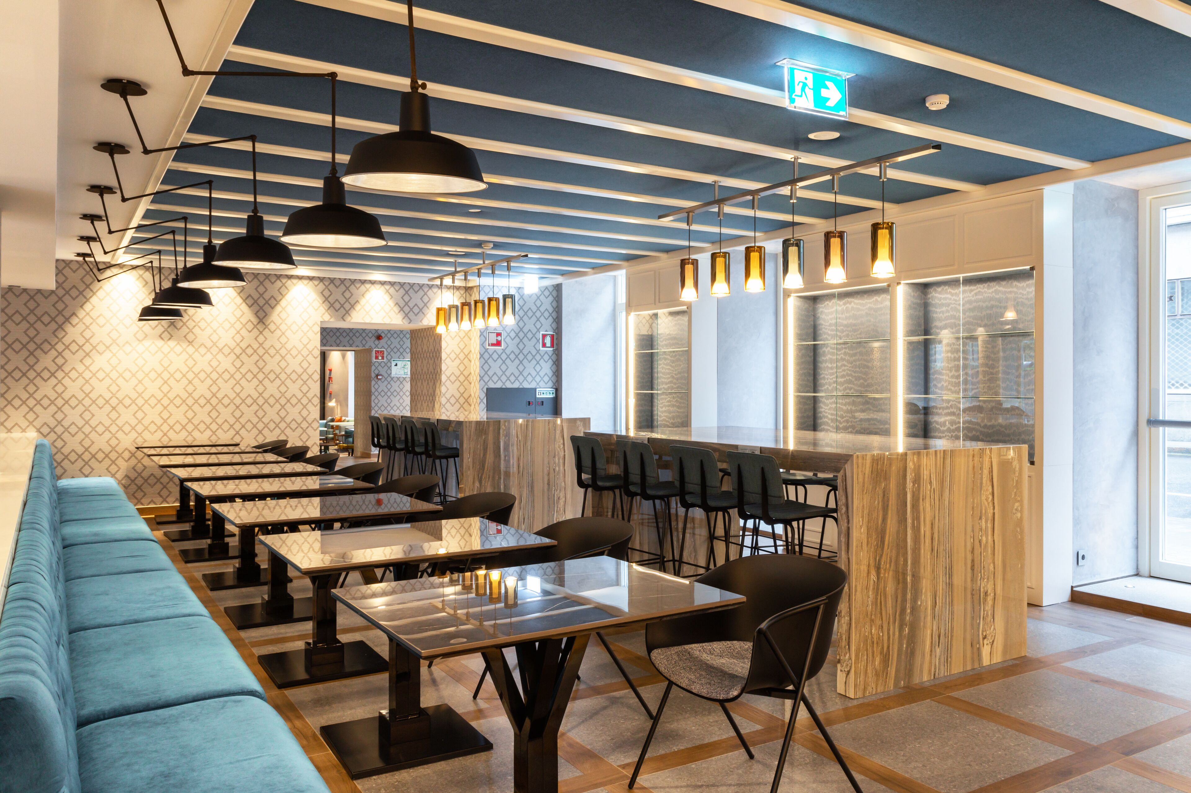 Un restaurante moderno con mesas comunitarias largas, asientos acolchados azules e iluminación colgante.