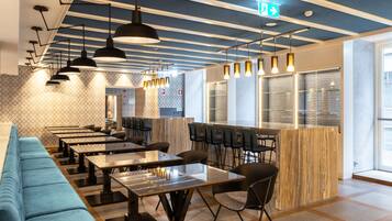 Un restaurante moderno con mesas comunitarias largas, asientos acolchados azules e iluminación colgante.