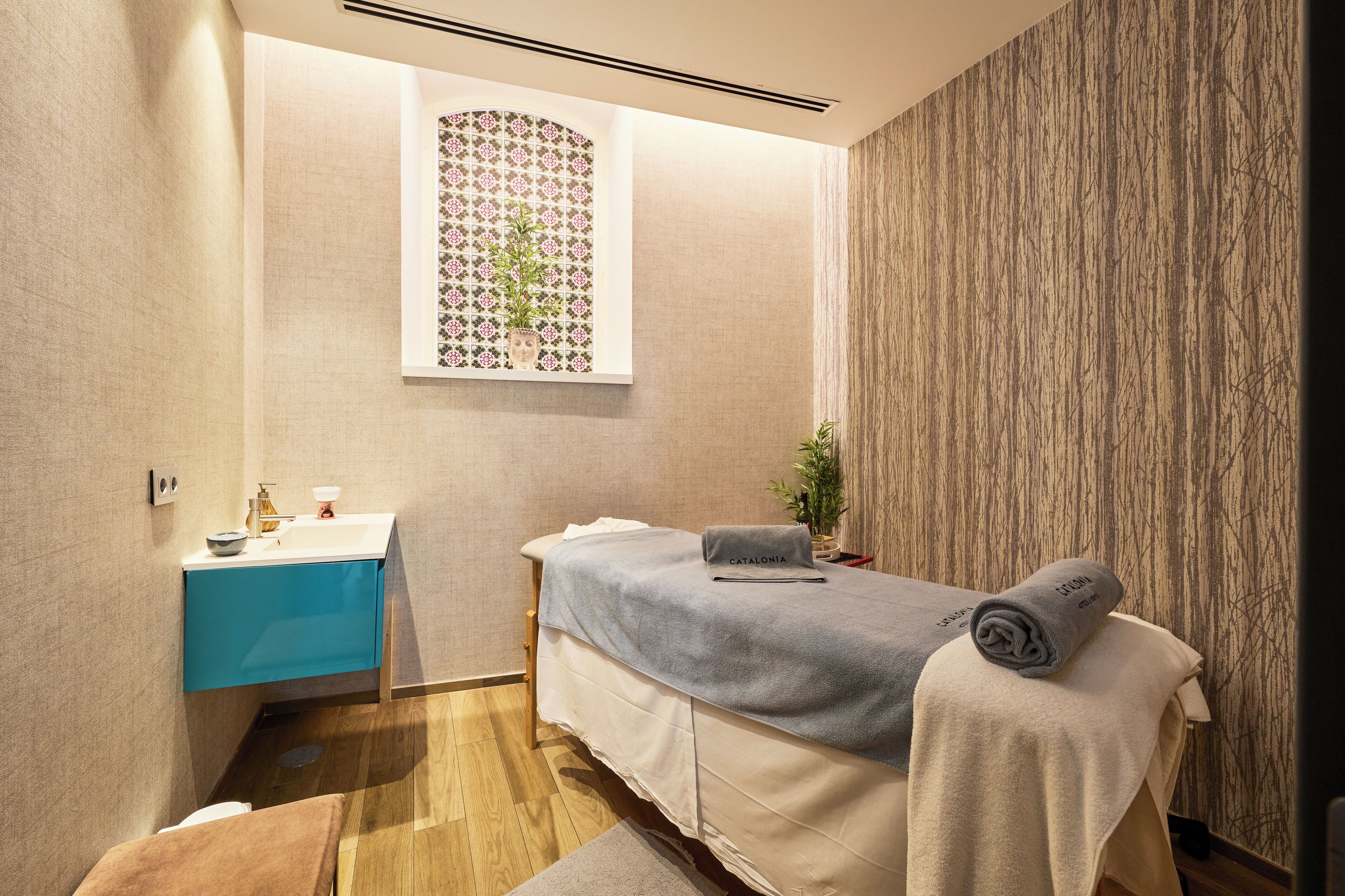 A spa room with a massage table, a blue vanity, and a decorative wall panel.