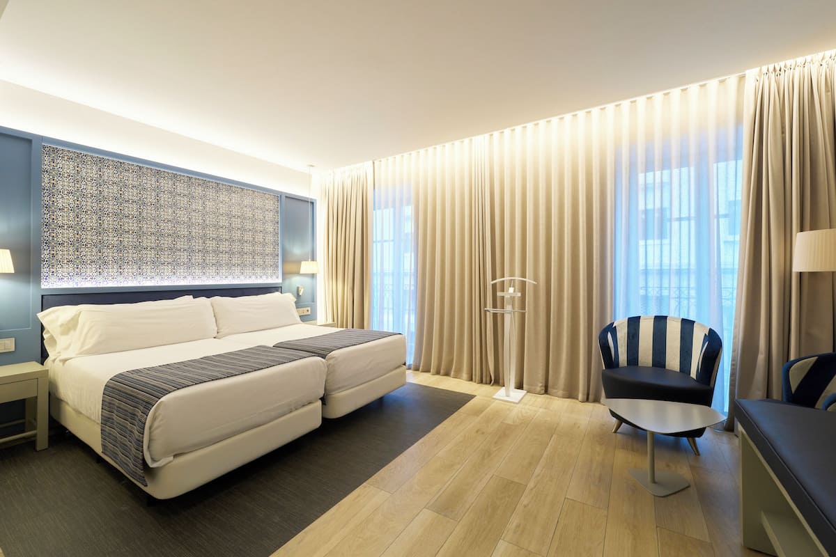 Ein modernes Hotelzimmer mit einem großen Bett, einem Schreibtisch, einem Stuhl und einem großen Fenster mit Vorhängen.