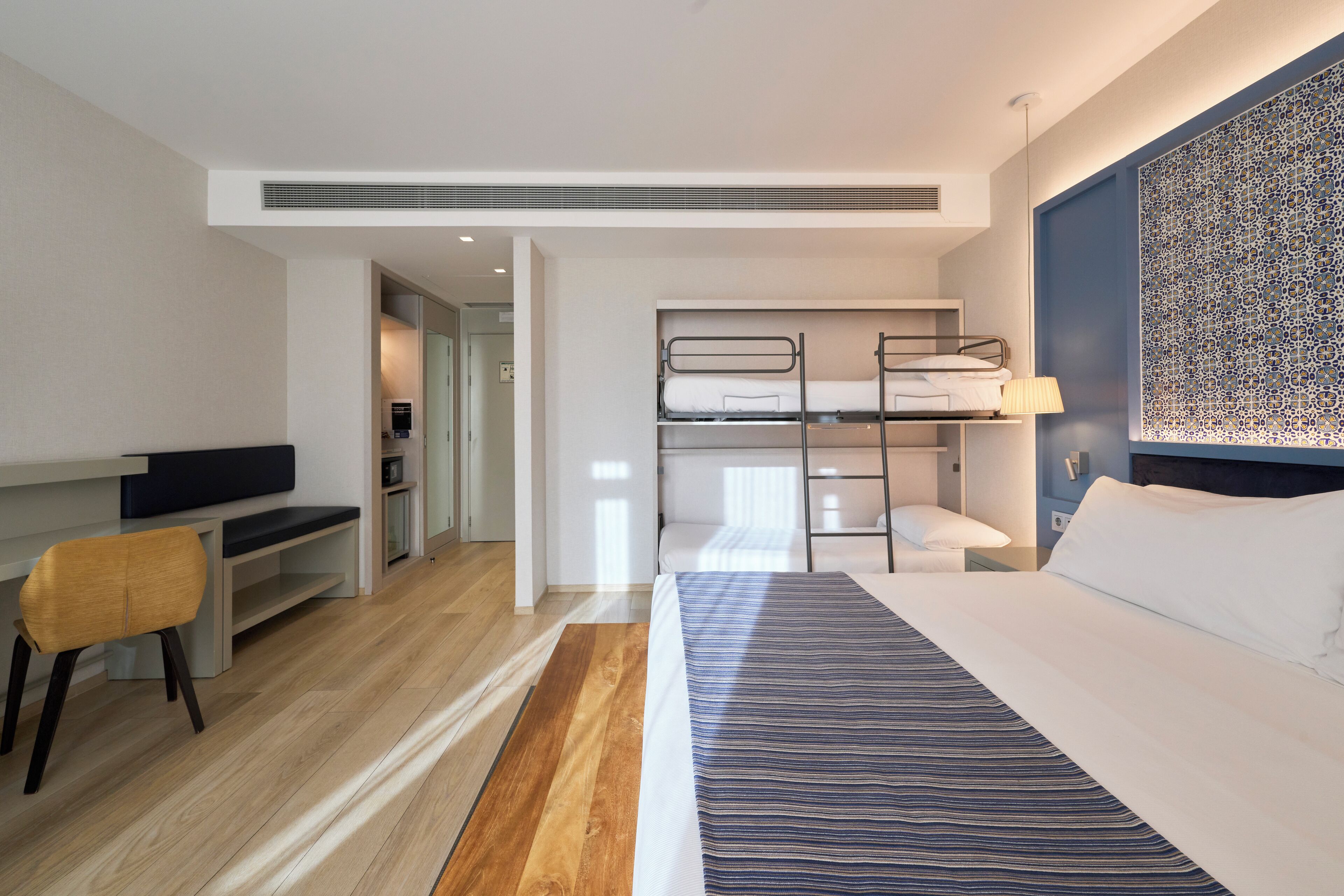Une chambre d’hôtel moderne avec un lit superposé, un bureau avec une chaise, une télévision et un mur décoré de motifs.