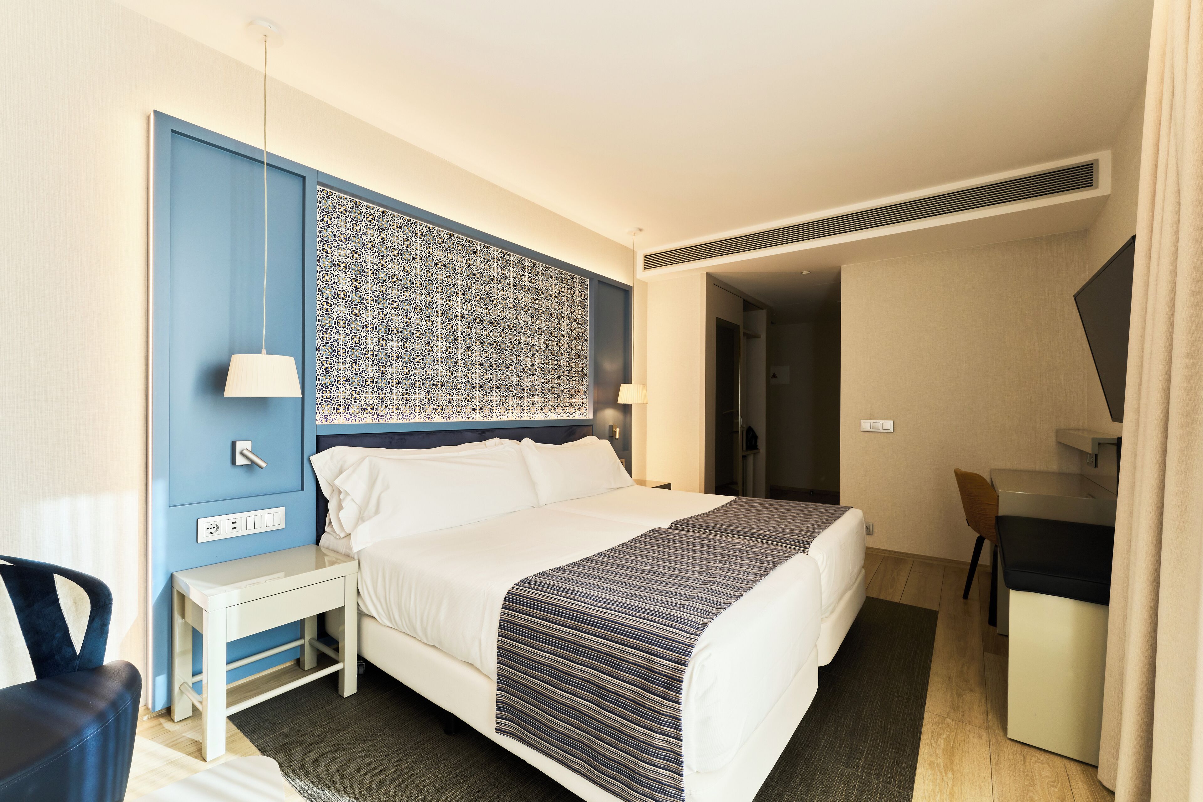 Een hotelkamer met een bed, nachtkastje, bureau, stoel en een behang met patroon.