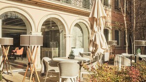 An outdoor seating area with tables and chairs, a potted plant, and a balcony with a railing.