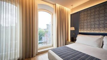 A hotel room with a large bed, a view of the outdoors through a window, and a decorative wall panel.