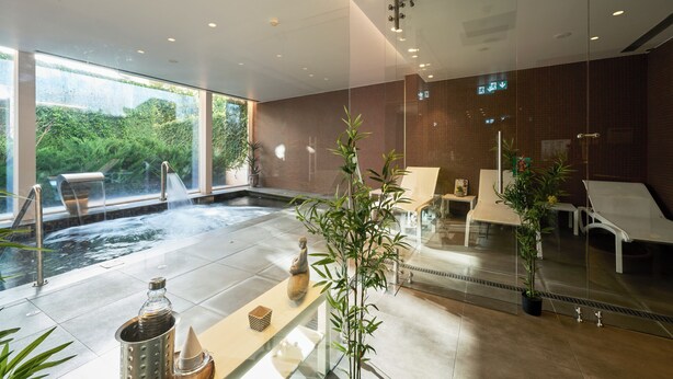 A modern spa with a hot tub, lounge chairs, and a glass wall offering a view of greenery.