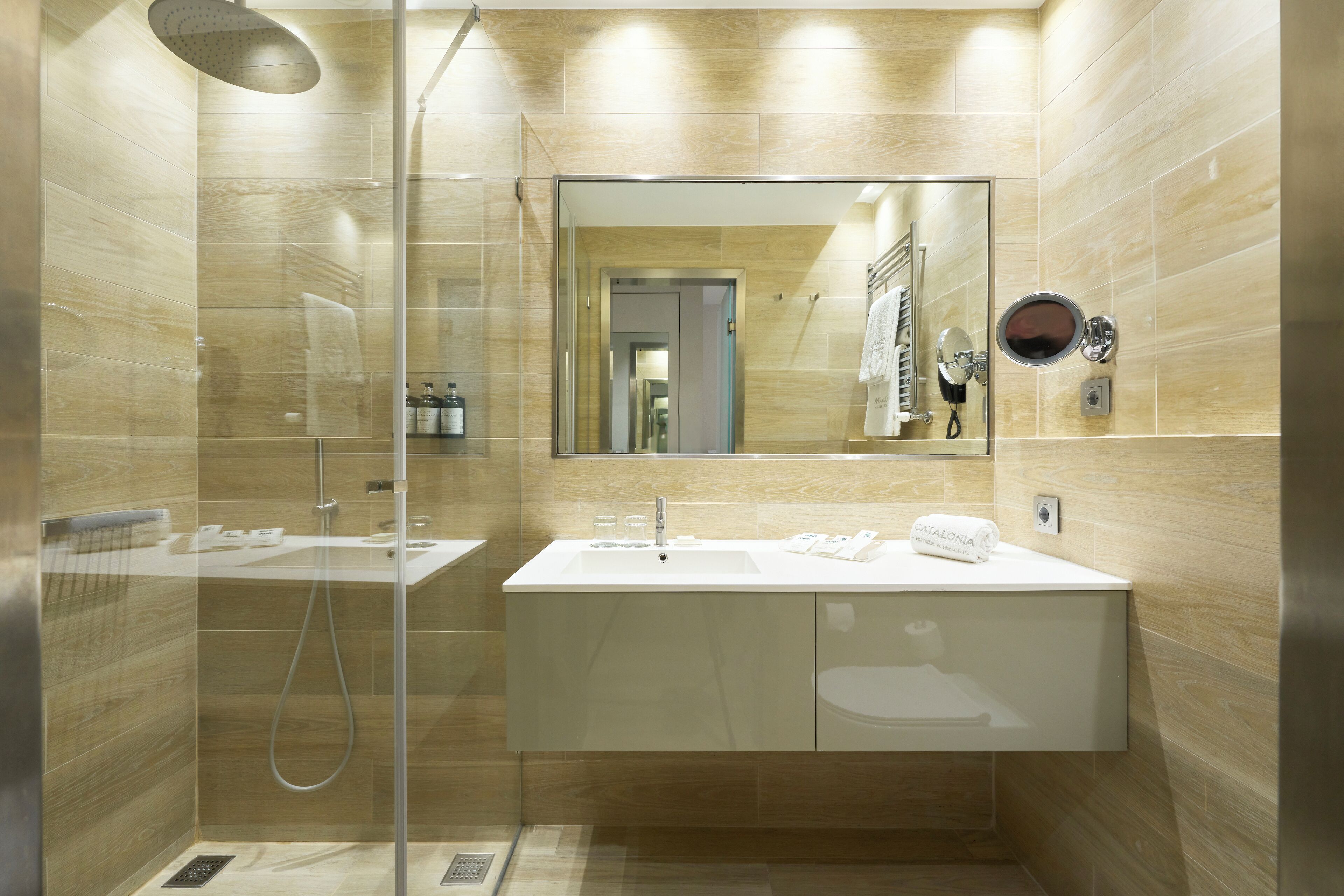 Un baño moderno con ducha envuelta en vidrio, un espejo grande y un tocador blanco.