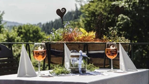 A table set outdoors with two glasses of wine, a heart-shaped decoration, and a small plant arrangement. - Hotel Merkurwald-Restaurant Wolpertinger (Baden-Baden)