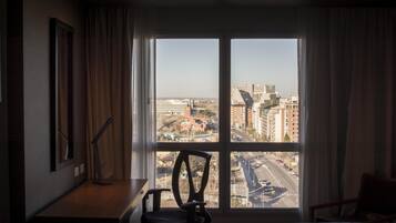 A hotel room with a large window offering a view of a cityscape.