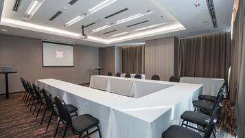 Una sala de conferencias con una larga mesa, filas de sillas, una pantalla de proyector y suelo alfombrado.