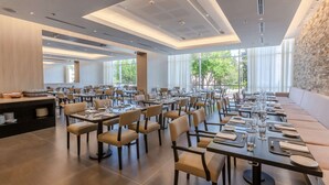 A spacious dining area with multiple tables and chairs, large windows, and a stone wall. - Hilton Garden Inn Neuquen (Neuquén)