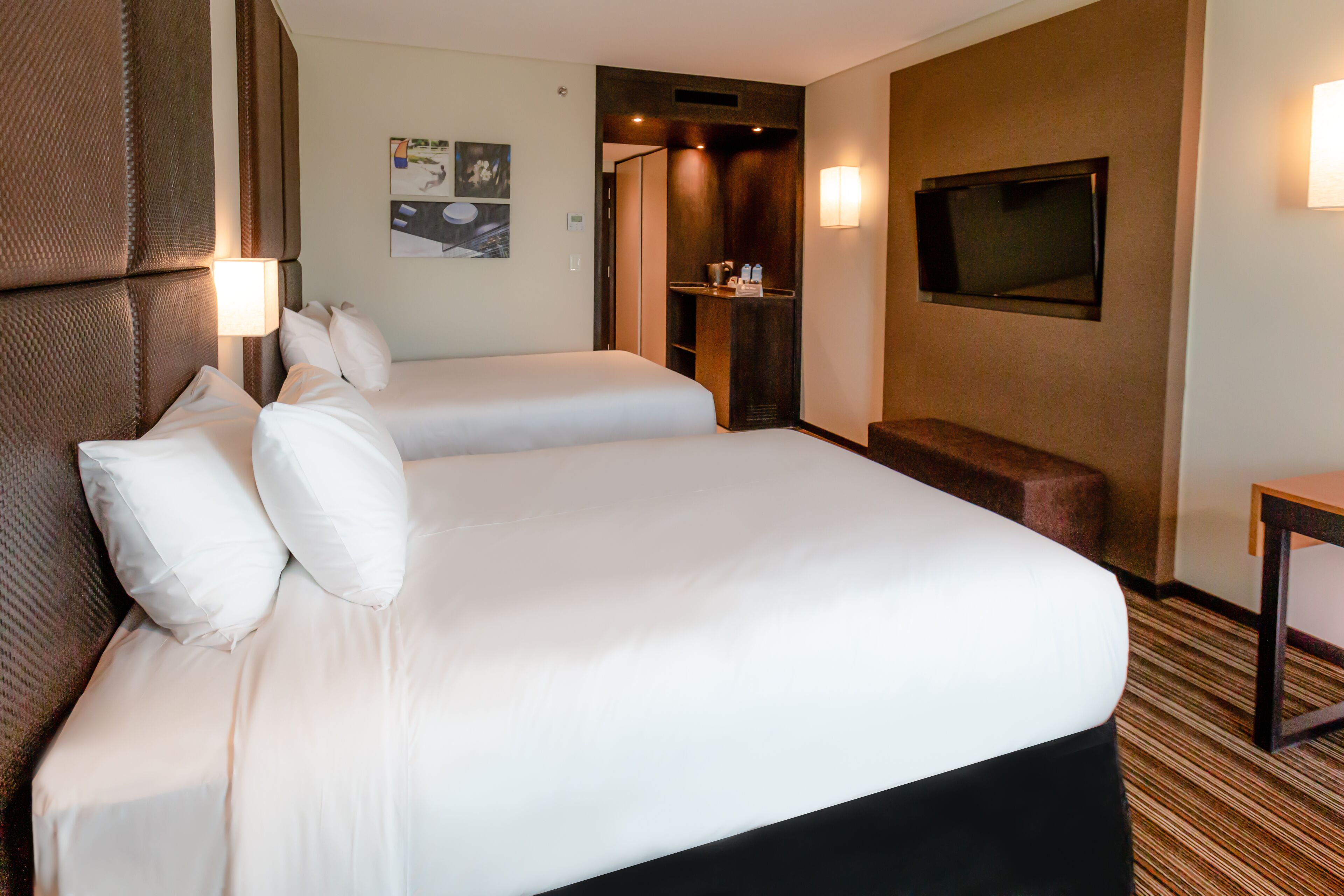 A hotel room with two beds, a TV, and a small seating area.