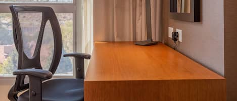 A modern office chair, a desk, a standing lamp, and a window with curtains.