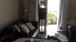 Un área de comedor con una mesa para dos, un sofá y vistas a espacios verdes.