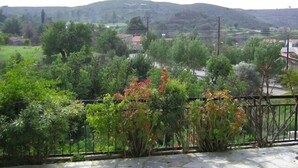 Un balcón con vista a un paisaje verde, que incluye árboles y un pueblo lejano.
