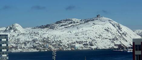 A coastal cityscape with a snow-covered hill, buildings, and a clear blue sky.