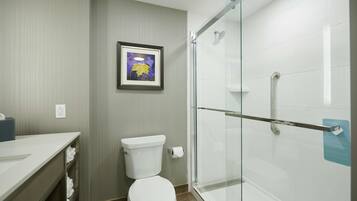 Un baño moderno con inodoro, cabina de ducha de vidrio y un cuadro en la pared.