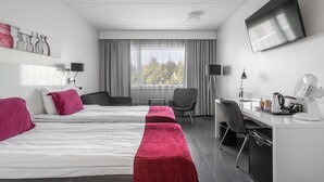 A hotel room with two beds, a desk, a chair, a TV, and a window with curtains. - Teatterihotelli Riihimäki (Riihimaki)