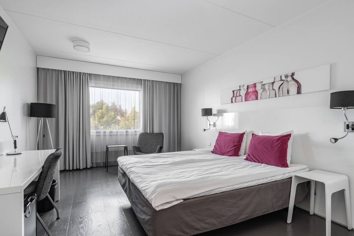 Ein modernes Hotelzimmer mit einem großen Bett, einem Schreibtisch, einem Stuhl und einem Fenster mit Vorhängen.