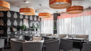 A modern lounge area with grey sofas, a coffee table, and orange pendant lights. - Teatterihotelli Riihimäki (Riihimaki)