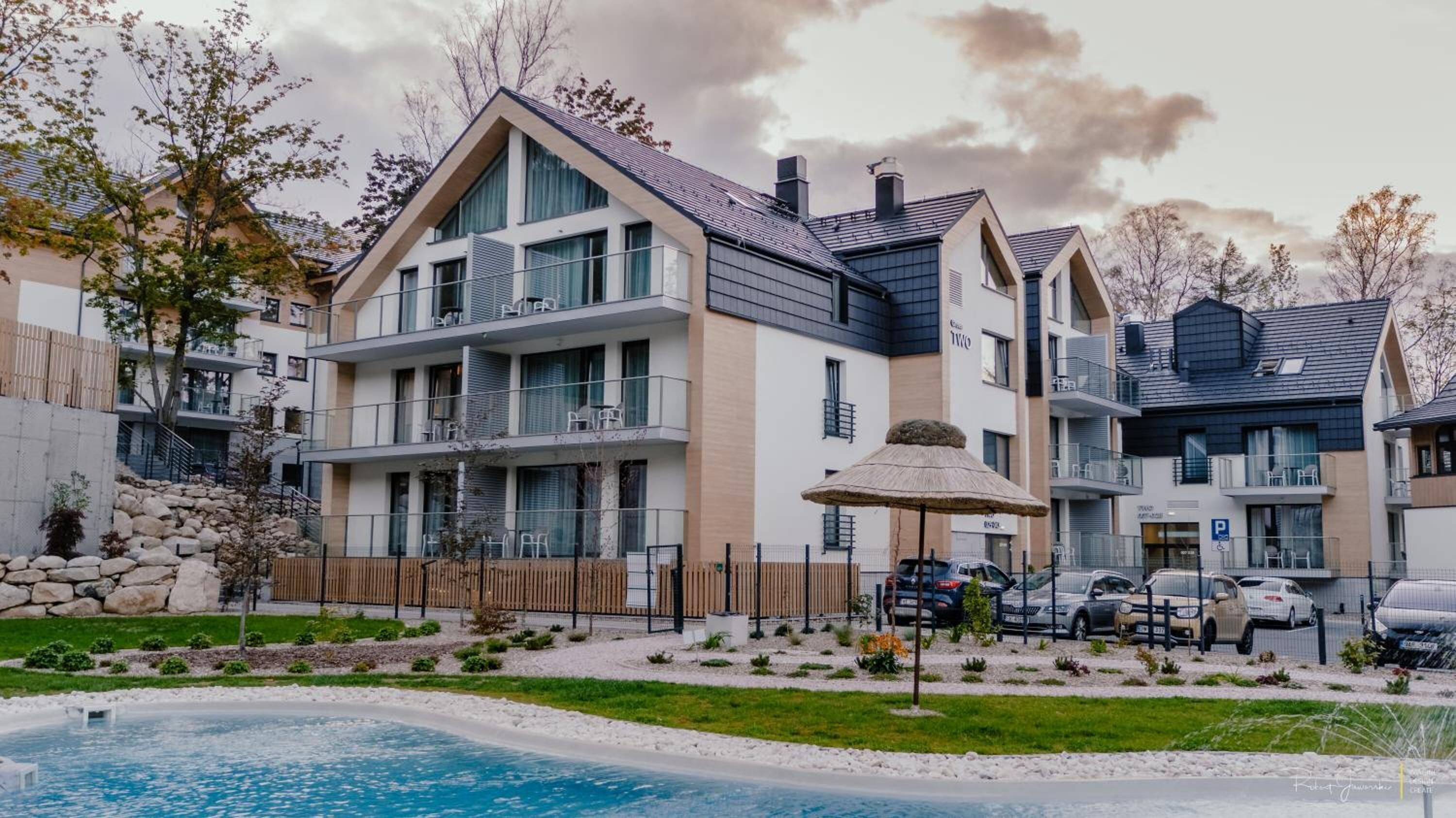 Un immeuble résidentiel moderne à plusieurs étages, doté de balcons, d’une piscine et d’un espace de stationnement.