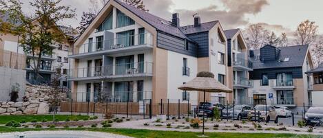 Un immeuble résidentiel moderne à plusieurs étages, doté de balcons, d’une piscine et d’un espace de stationnement.