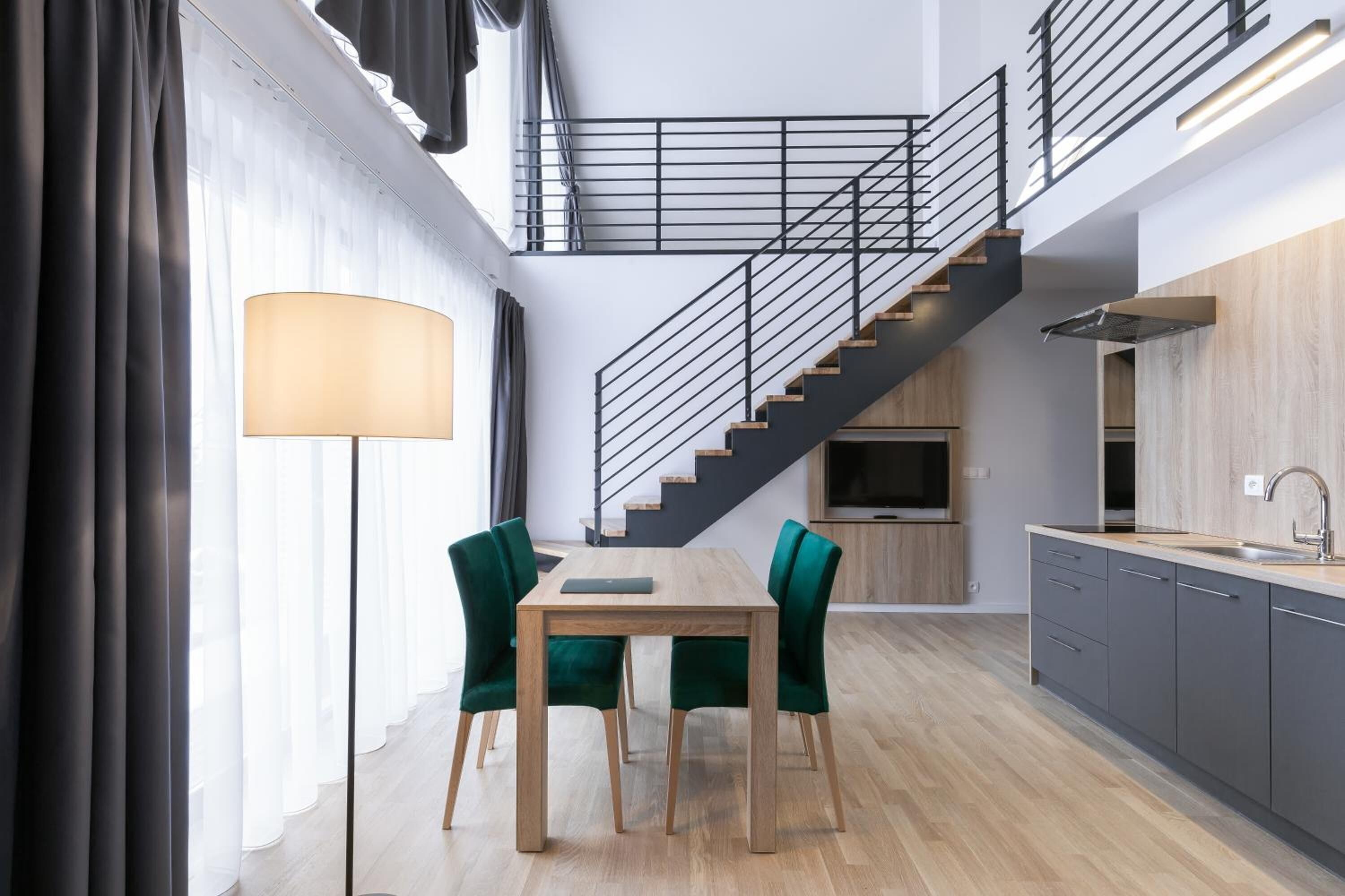 A modern kitchen with a wooden table and chairs, a staircase, and a built-in oven.