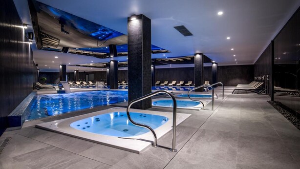 A modern indoor pool area with multiple hot tubs and lounge chairs, featuring a sleek design and ample seating. - Green Apartments (Karpacz)