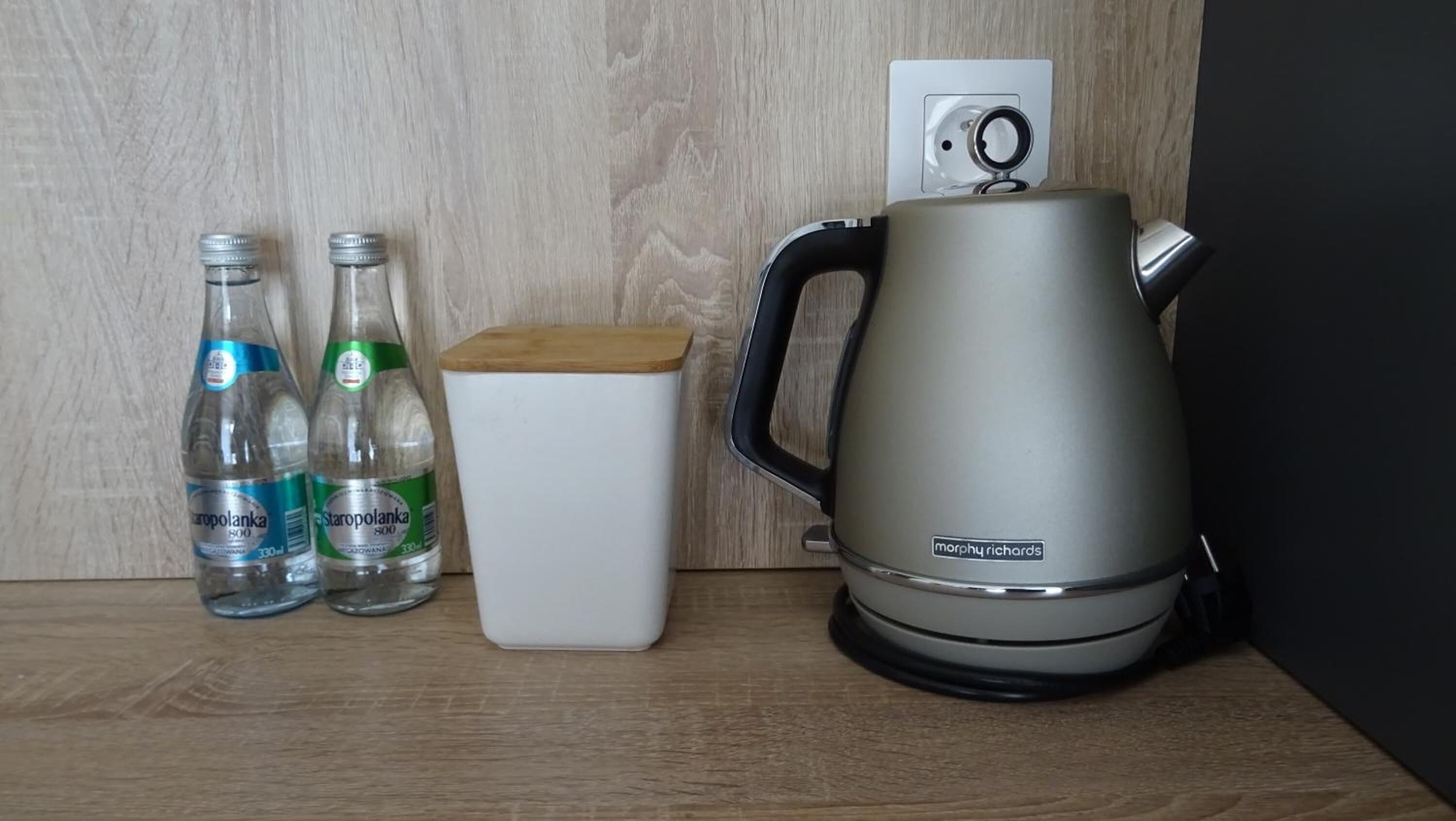 A kitchen counter with a kettle, two bottles of water, and a white container.