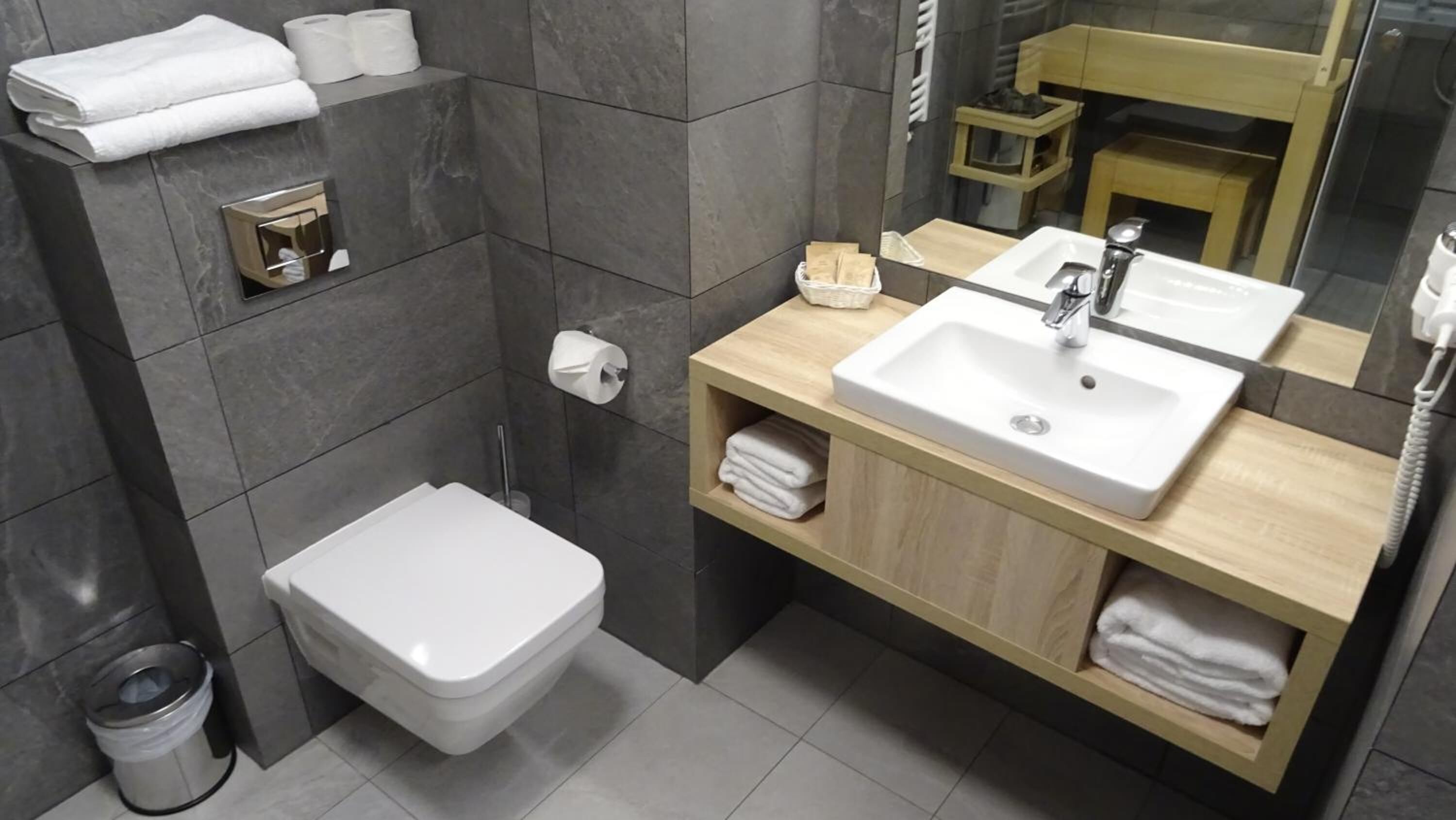 A modern bathroom with a white toilet, a sink with a mirror above it, and a towel rack with towels.