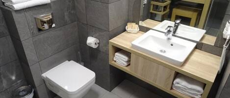 A modern bathroom with a white toilet, a sink with a mirror above it, and a towel rack with towels.