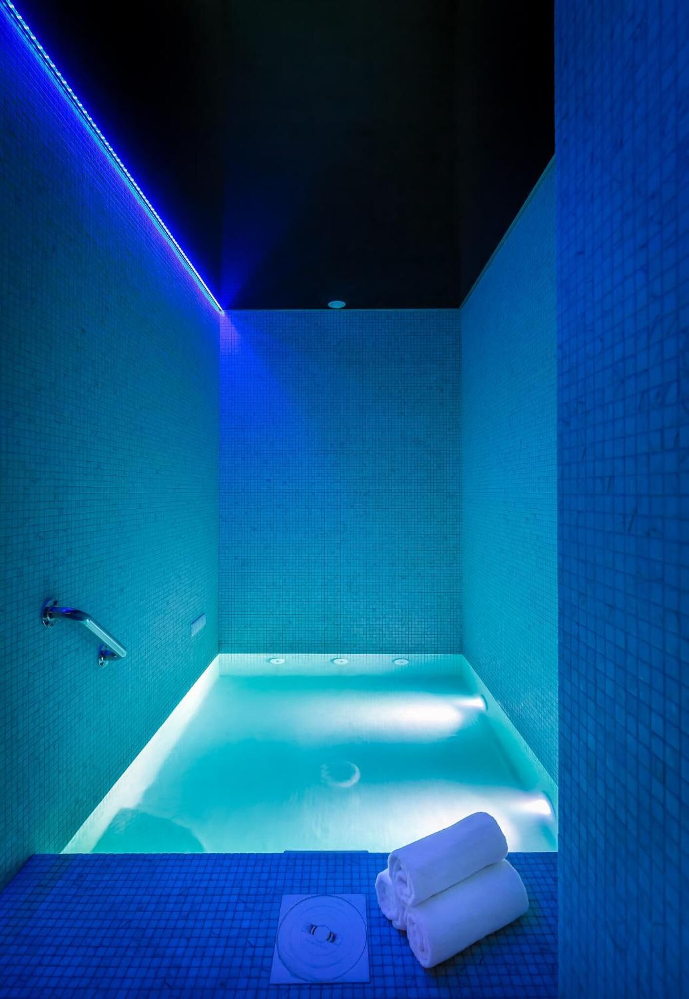 Un baño moderno con una bañera grande, iluminación LED azul y un perchero para toallas.