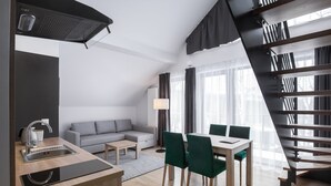 A modern kitchen with a built-in stove, a dining area with a table and chairs, a sofa, and a staircase. - Green Apartments (Karpacz)