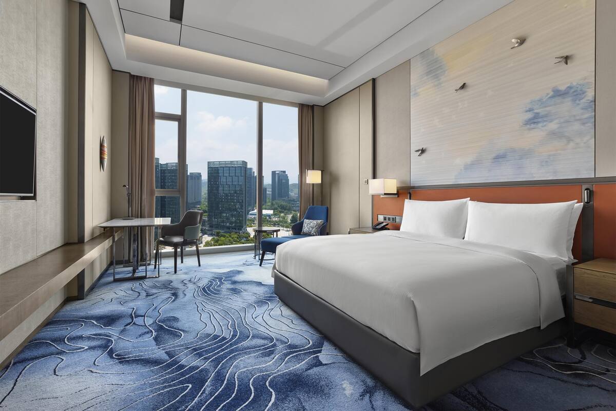 Une chambre d’hôtel avec un grand lit, un bureau et une chaise. La fenêtre offre une vue sur la ville.