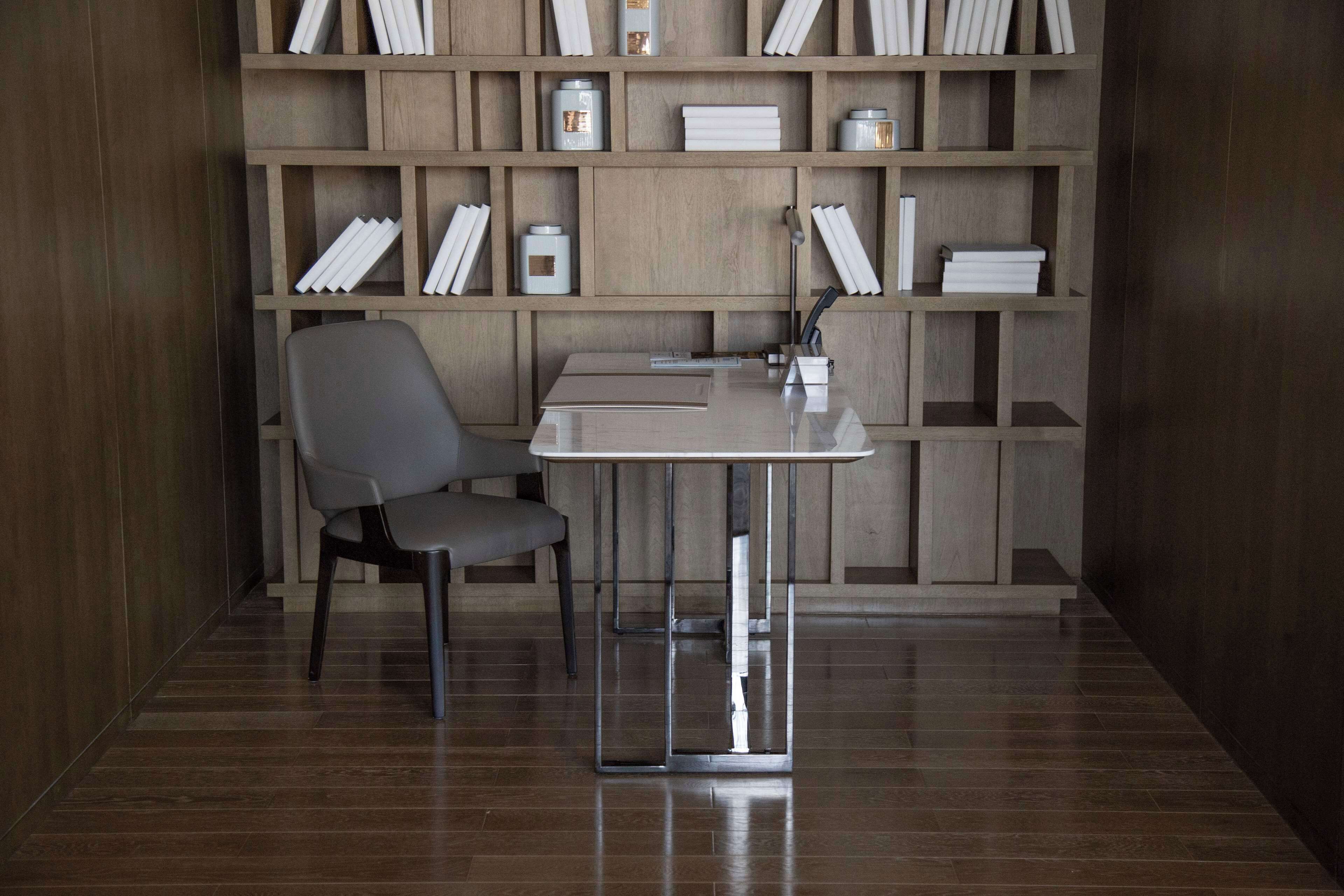 A modern office space with a desk, chair, and a wooden bookshelf filled with books and decorative items.