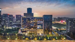 Um hotel moderno com fachada de vidro, vários andares e um terraço no telhado.