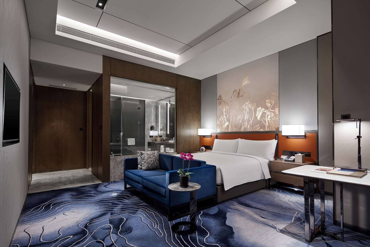 Une chambre d’hôtel moderne, équipée d’un lit, d’un canapé, d’une petite table avec une plante et d’un bureau avec une lampe.