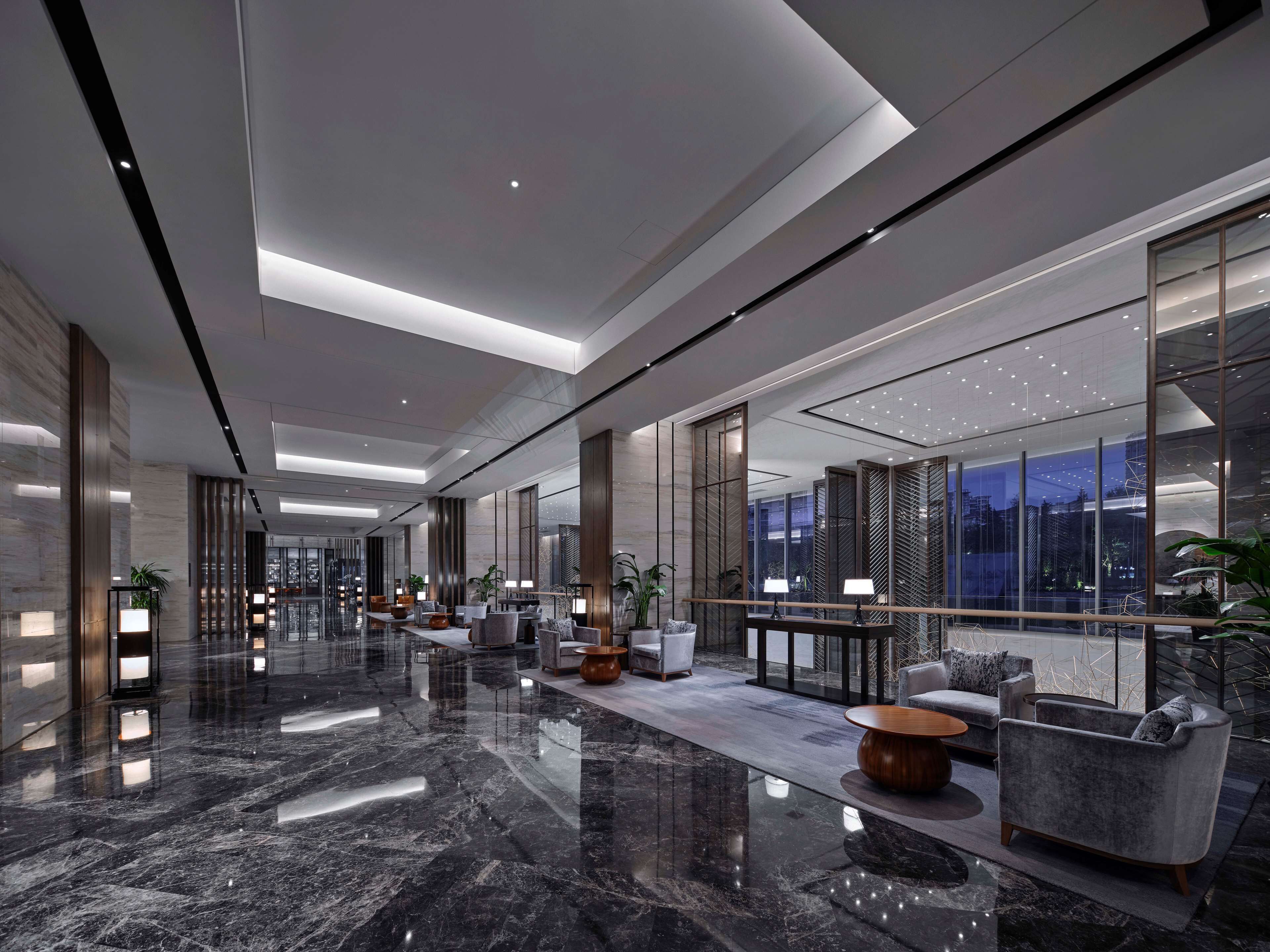 A spacious lobby with a polished marble floor, seating areas with modern furniture, and large windows offering a view of the cityscape.