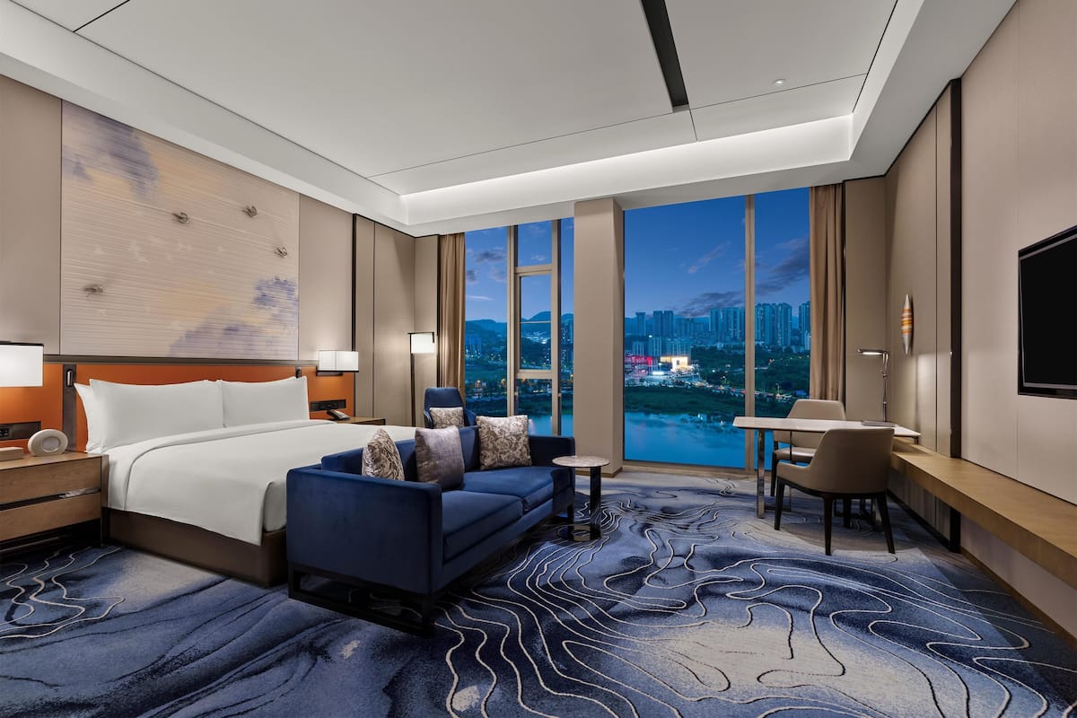 Une chambre d’hôtel moderne dotée d’un grand lit, d’un canapé, d’un bureau et offrant une vue sur le paysage urbain.
