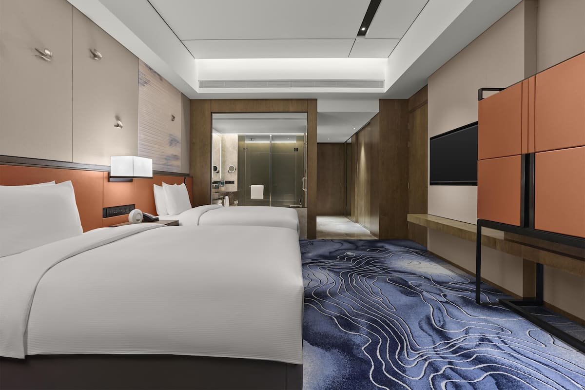 Une chambre d’hôtel moderne équipée de deux lits, d’un grand miroir, d’une télévision et d’une salle de bain avec douche et toilettes.