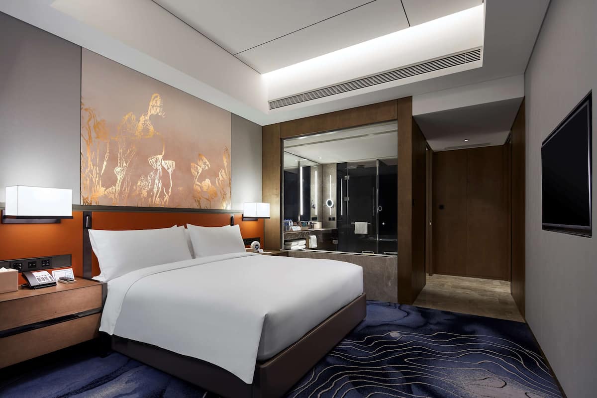 Une chambre d’hôtel moderne avec un grand lit, des lampes de chevet, un bureau avec un téléphone et un grand miroir.