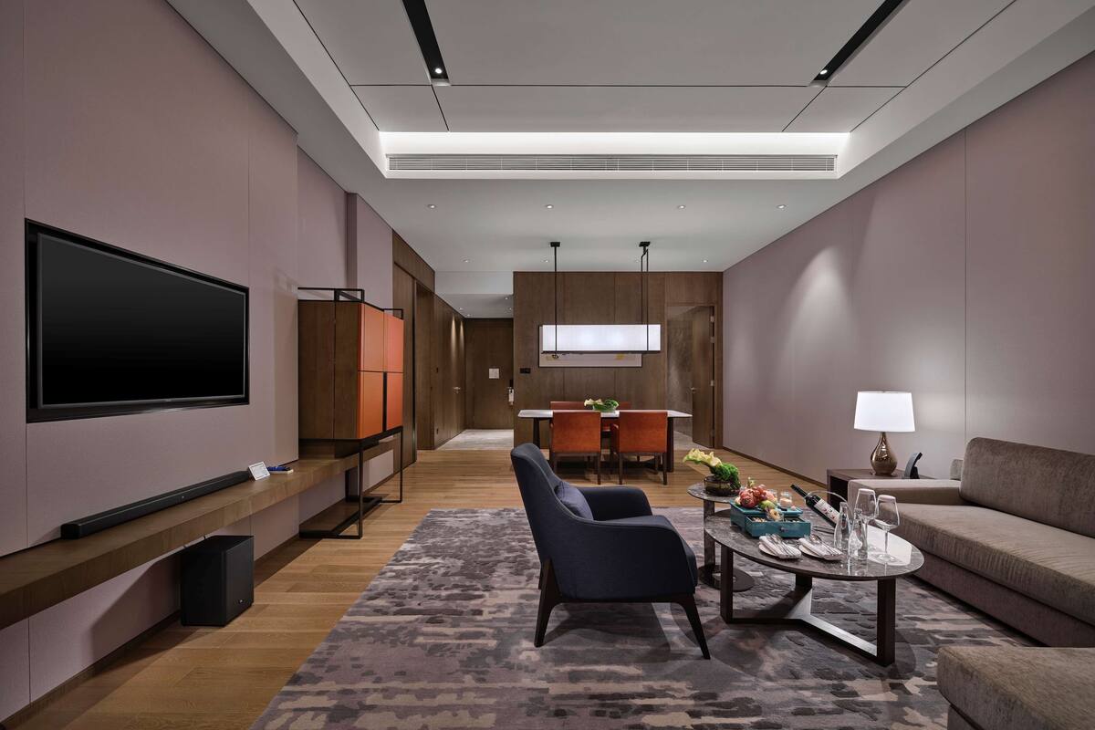 Un salon moderne avec un téléviseur à écran plat, un canapé, une table basse avec des boissons, et un coin repas à l’arrière-plan.