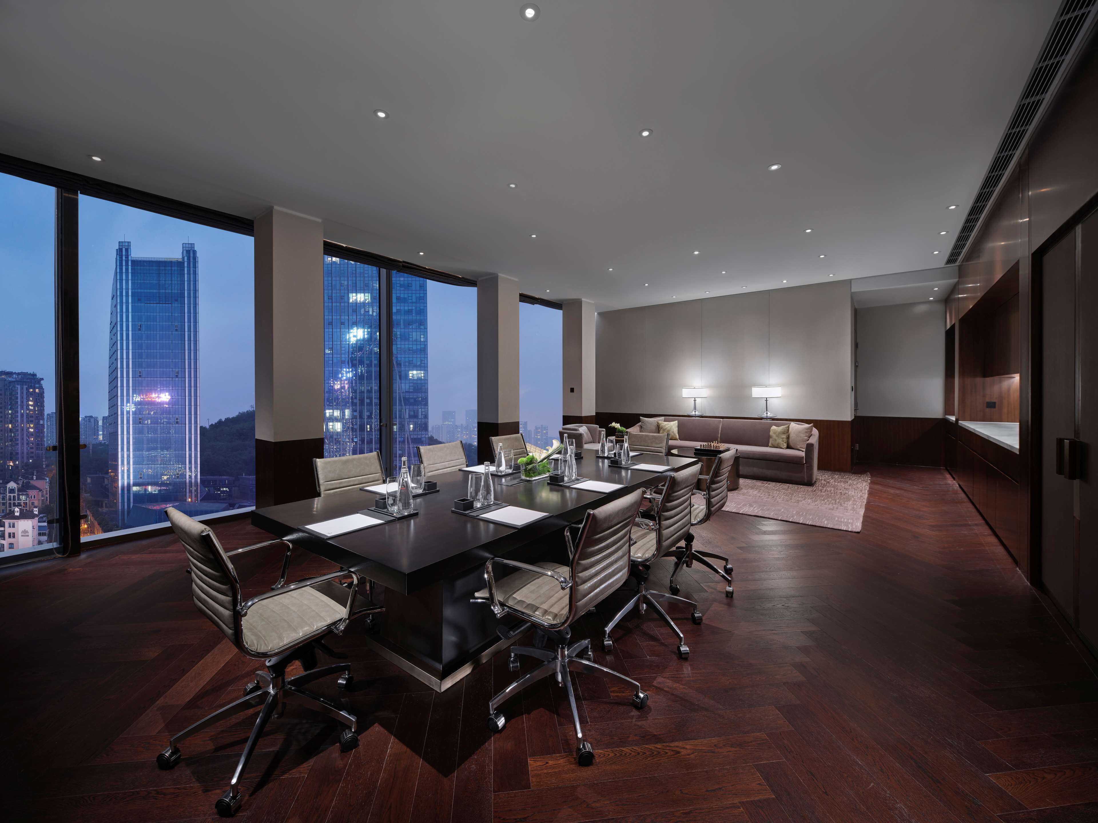 A modern conference room with a large table, chairs, and a sofa. It features large windows with a city view.
