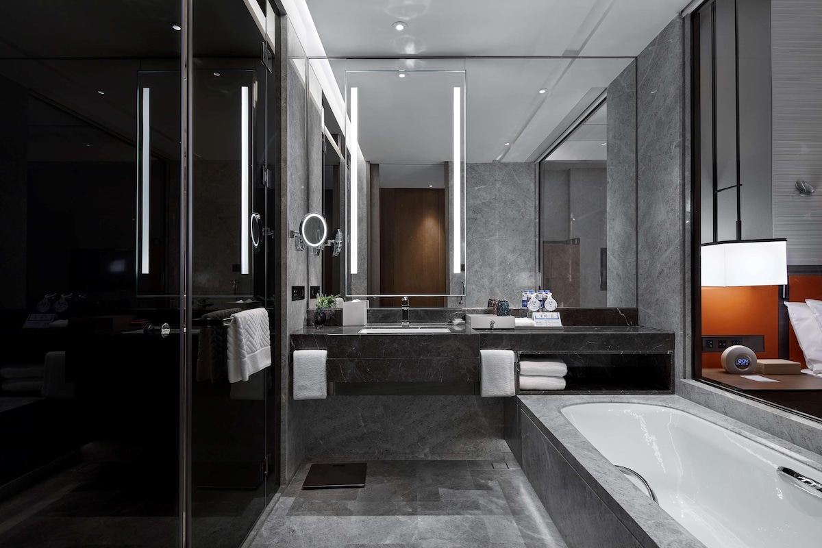 A modern bathroom with a glass shower enclosure, a large mirror, a bathtub, and a vanity with a sink and towel rack.