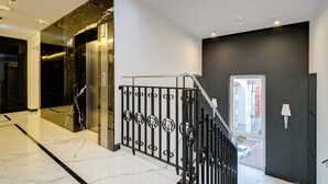 A modern interior with a marble floor, a staircase with a metal railing, and a view of the outside through a window.