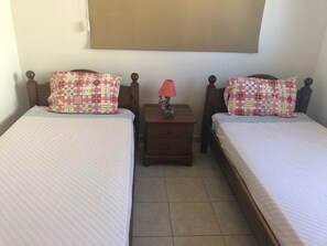 Una camera da letto con due letti singoli, ognuno con un cuscino decorato e un comodino con una lampada.